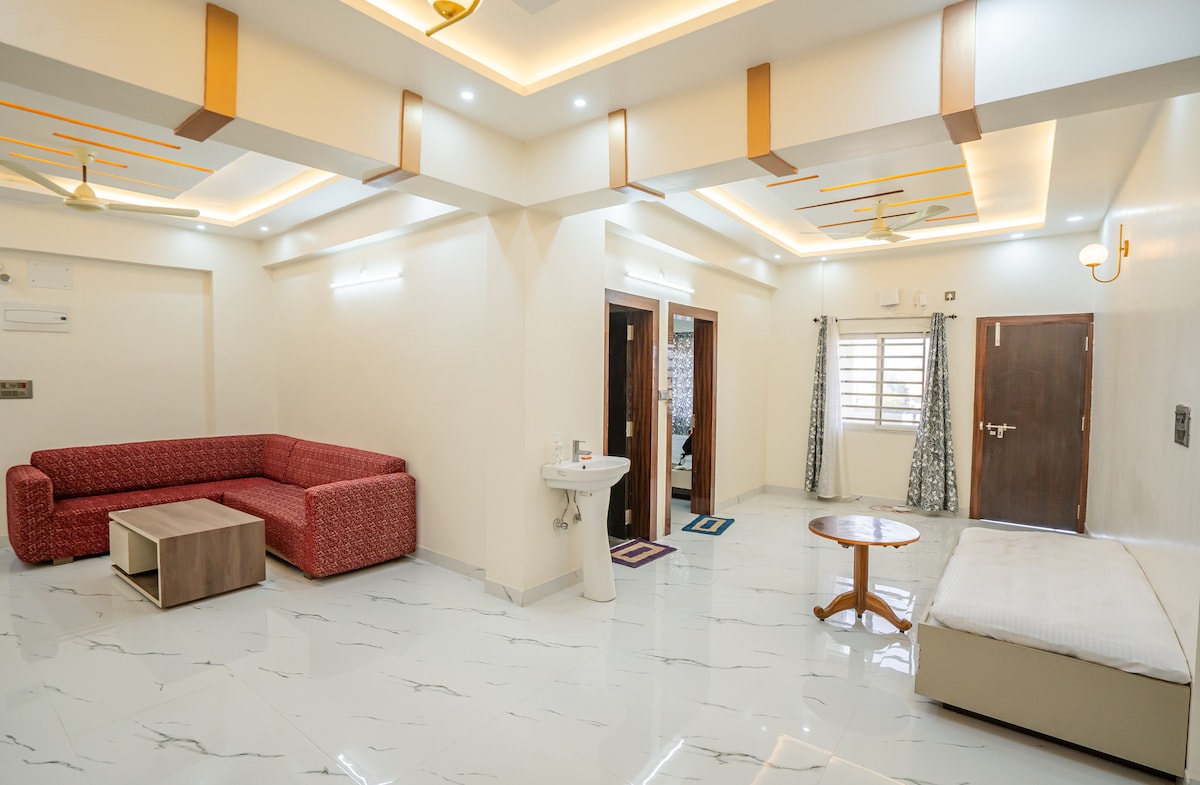 The spacious living area features elegant ceiling designs and recessed lighting, enhancing the welcoming environment. A red sectional sofa and a wooden coffee table are positioned for comfort. Doorways lead to the bedrooms, while natural light filters through the window treatments.