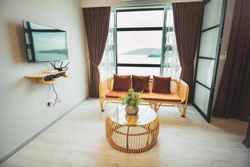 A comfortable sitting area features a rattan sofa adorned with cushions, complemented by a round glass coffee table. Large windows allow views of the ocean and illuminate the space with natural light, while soft drapes frame the windows.