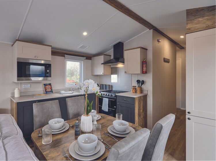 A modern kitchen and dining area feature sleek cabinetry and a comfortable table set with four plates and glasses. Natural light enters through a nearby window, illuminating the space. A microwave and stove are positioned for convenience, complemented by a soft couch nearby.