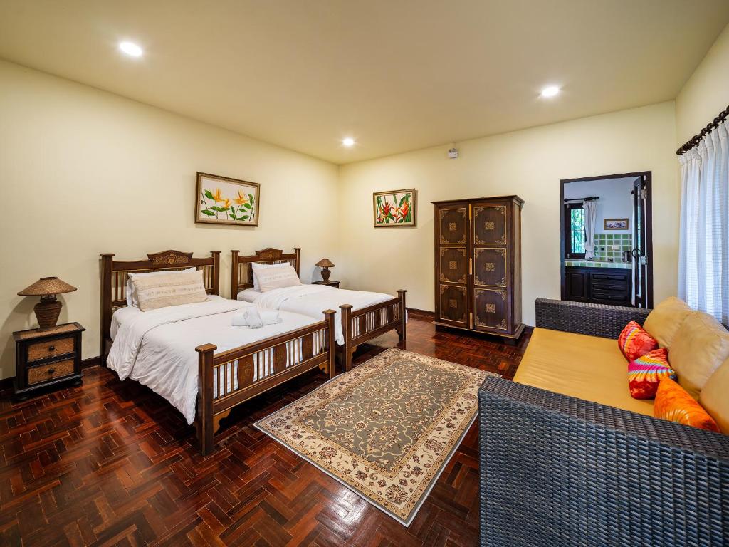 A spacious room features two wooden beds with crisp linens, complemented by decorative pillows. A large area rug lies on the polished wooden floor. Nearby, a woven sofa offers additional seating, while framed art pieces adorn the walls, enhancing the overall aesthetic.