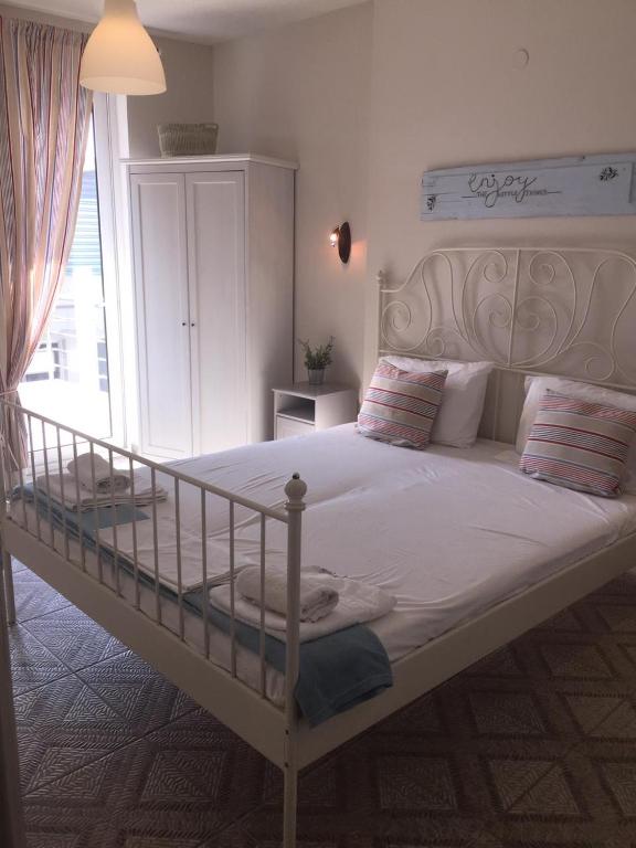 A bright bedroom features a white metal bed with crisp linens and decorative pillows. Light streams in through a glass door leading to a small balcony. A white wardrobe provides storage, while a subtle piece of wall art contributes to the calming ambiance.