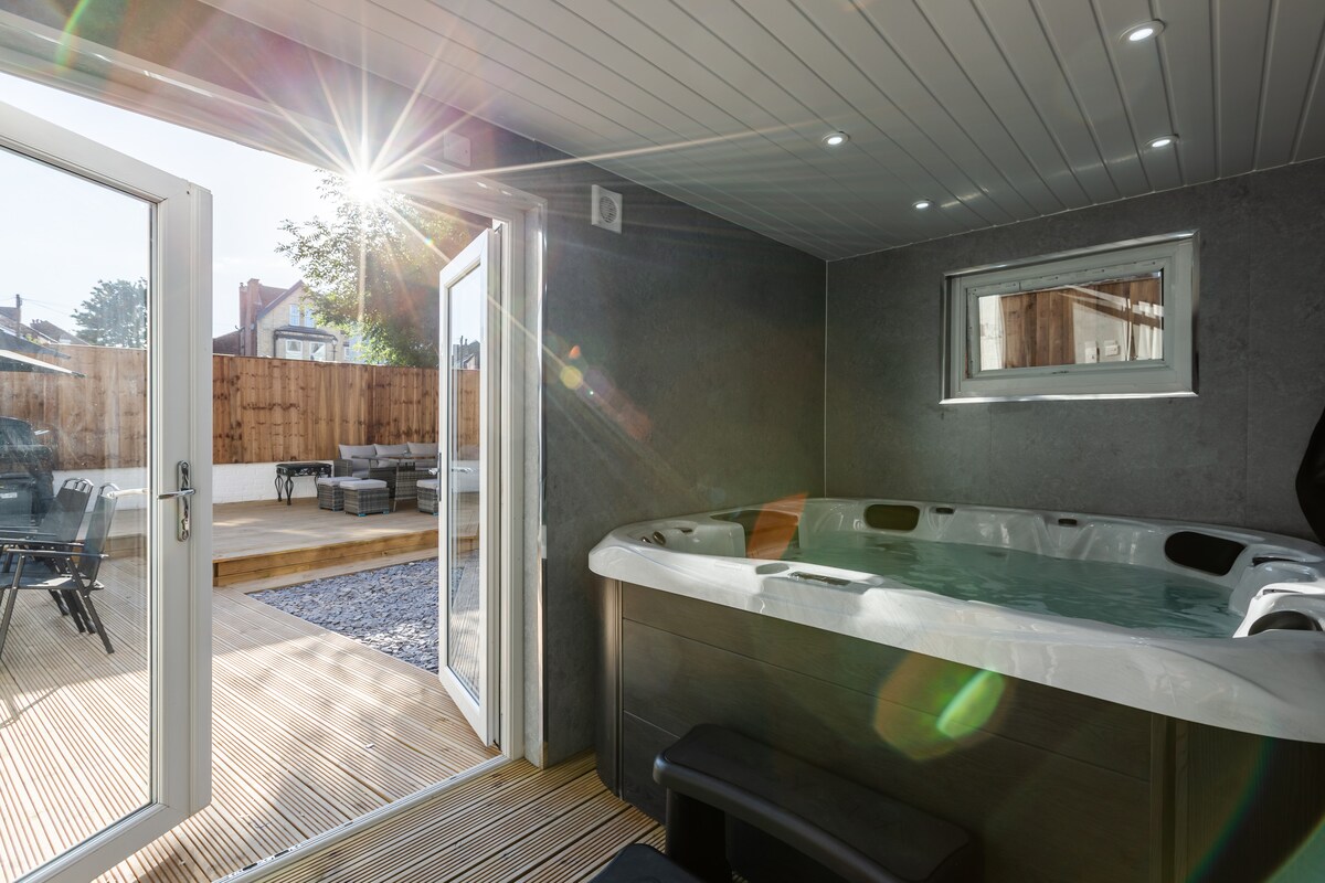 A private spa room features a hot tub, surrounded by wood paneling and soft lighting. The space is illuminated by sunlight streaming in through open doors, leading to a patio area furnished with outdoor seating.