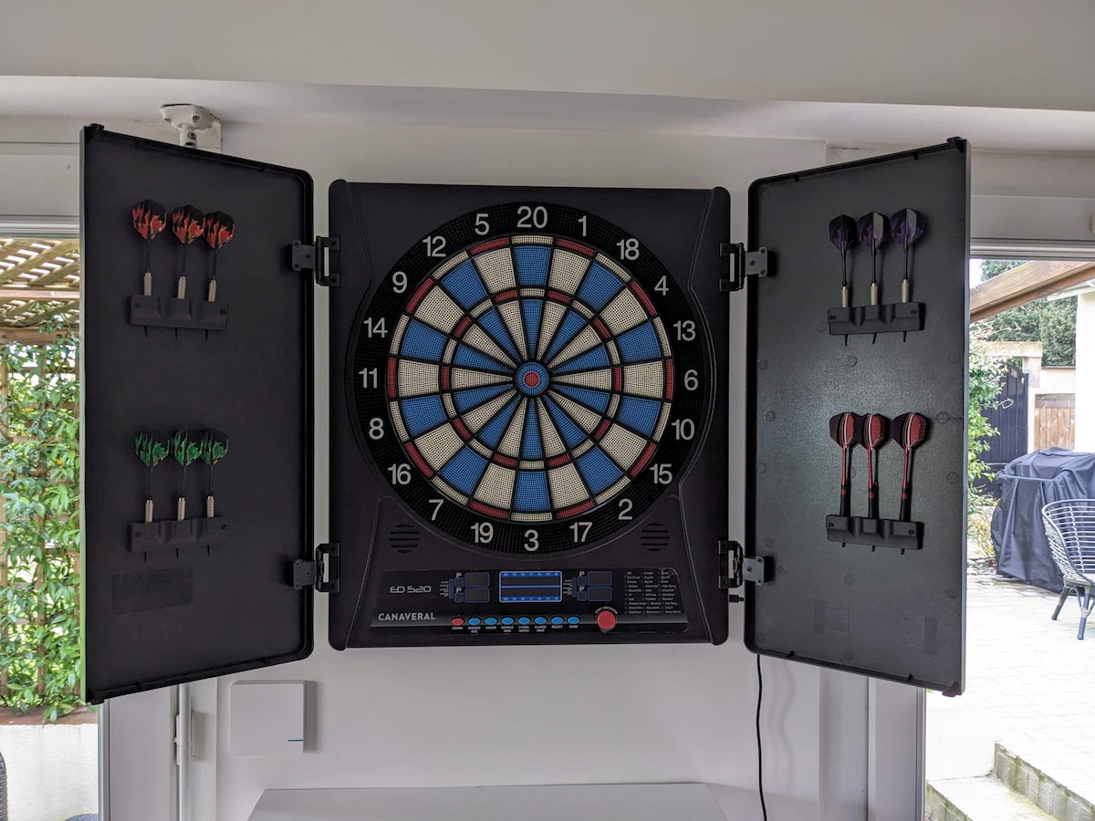 An electronic dartboard is mounted on the wall, flanked by two cabinets holding sets of colorful dart arrows. The board displays numbered segments in vibrant hues, offering a space for recreational activities.