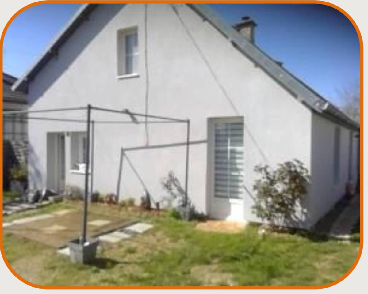 An exterior view of the house is displayed, featuring a simple white facade and a neatly landscaped courtyard. A clothesline stands in the yard, and large windows allow natural light to enter. The roofline is gently sloped, and greenery complements the structure.