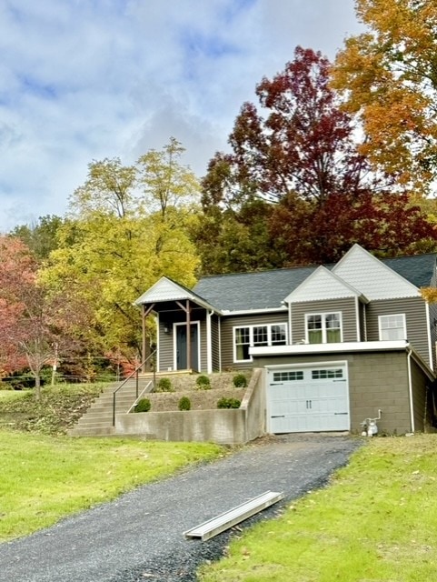 A cottage is set against a backdrop of autumn foliage, featuring a welcoming front porch and a grassy yard. The driveway leads up to a garage, with colorful trees surrounding the property, highlighting the serene and natural environment.