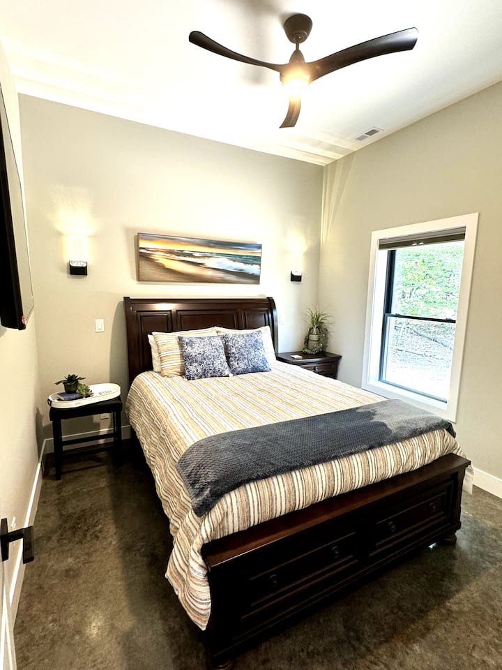 Queen bed with sheets, comforter, and four pillows. Night stand and end table. Wall sconces on each side of the bed as well as a smartTV located in the room and can be pulled out from the wall and adjusted for viewing.