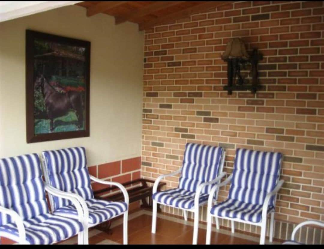 A covered seating area is furnished with four white chairs featuring blue and white striped cushions. A small wooden table is positioned in the center. The wall is accented by a large framed artwork depicting a horse and is complemented by a decorative lamp.