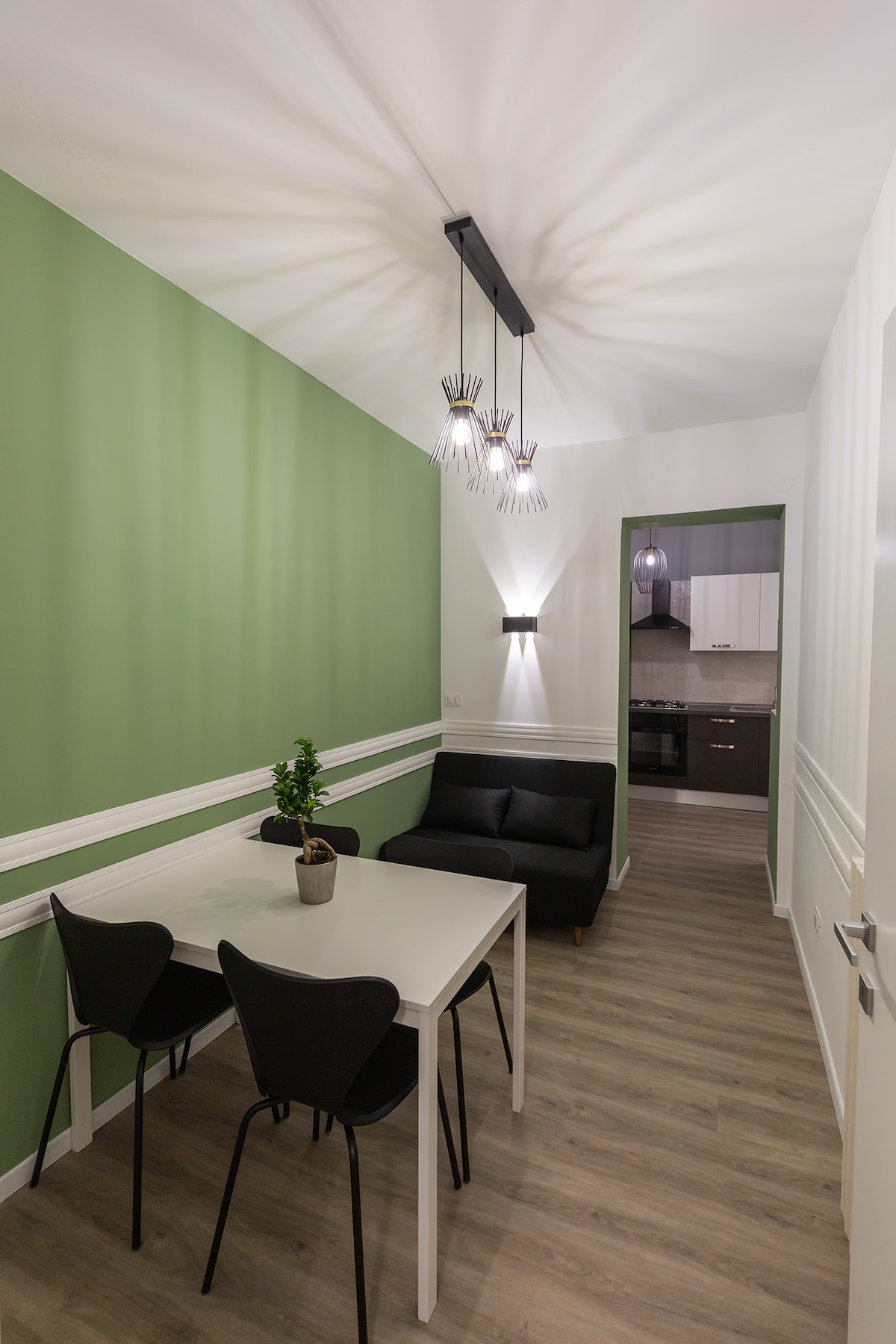 A dining area is highlighted by a white table and black chairs, accompanied by a comfortable dark sofa. Clean lines are enhanced by a unique ceiling light fixture casting a patterned shadow. Light green walls add a fresh touch, creating an inviting space.