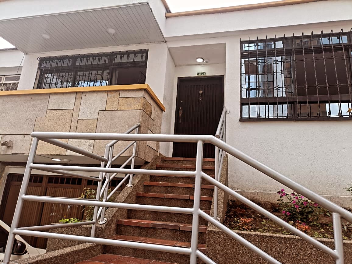 An entrance is showcased with a set of stairs leading up to a wooden door, bordered by a stone wall. Metal railings provide support, and flower beds add subtle color along the steps. Natural light illuminates the area, enhancing visibility.