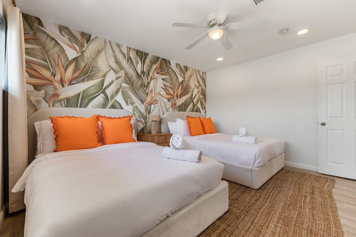 Svetlá spálňa s dvoma samostatnými posteľami, výraznými vankúšmi a hravým umeleckým nástenným dekorom.