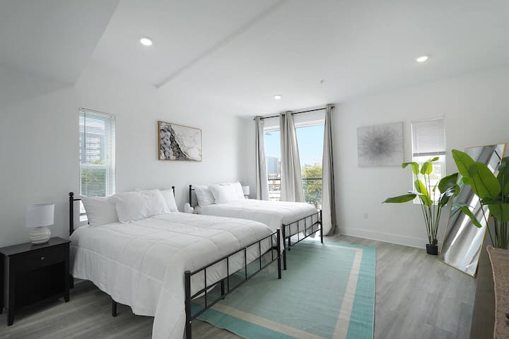 Esta luminosa recámara cuenta con dos camas cómodas con sábanas blancas y limpias y una gran planta verde que aporta un toque fresco. Varias ventanas y una puerta de vidrio dejan entrar mucha luz, lo que hace que la habitación se sienta abierta y espaciosa.