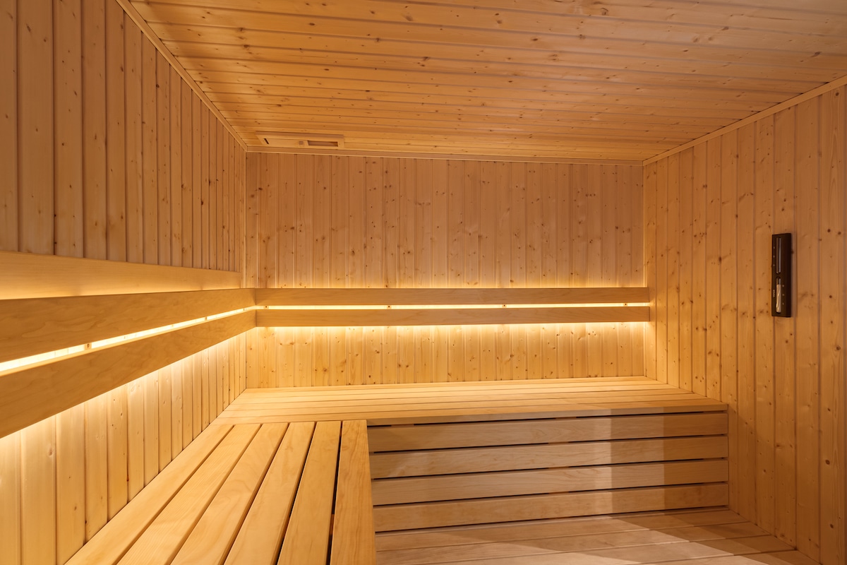 A serene sauna space is presented with wooden paneling and benches. Soft lighting highlights the natural wood grain, creating a calm environment. The room offers a minimalist design, with ample seating and a consistent atmosphere, suitable for relaxation.