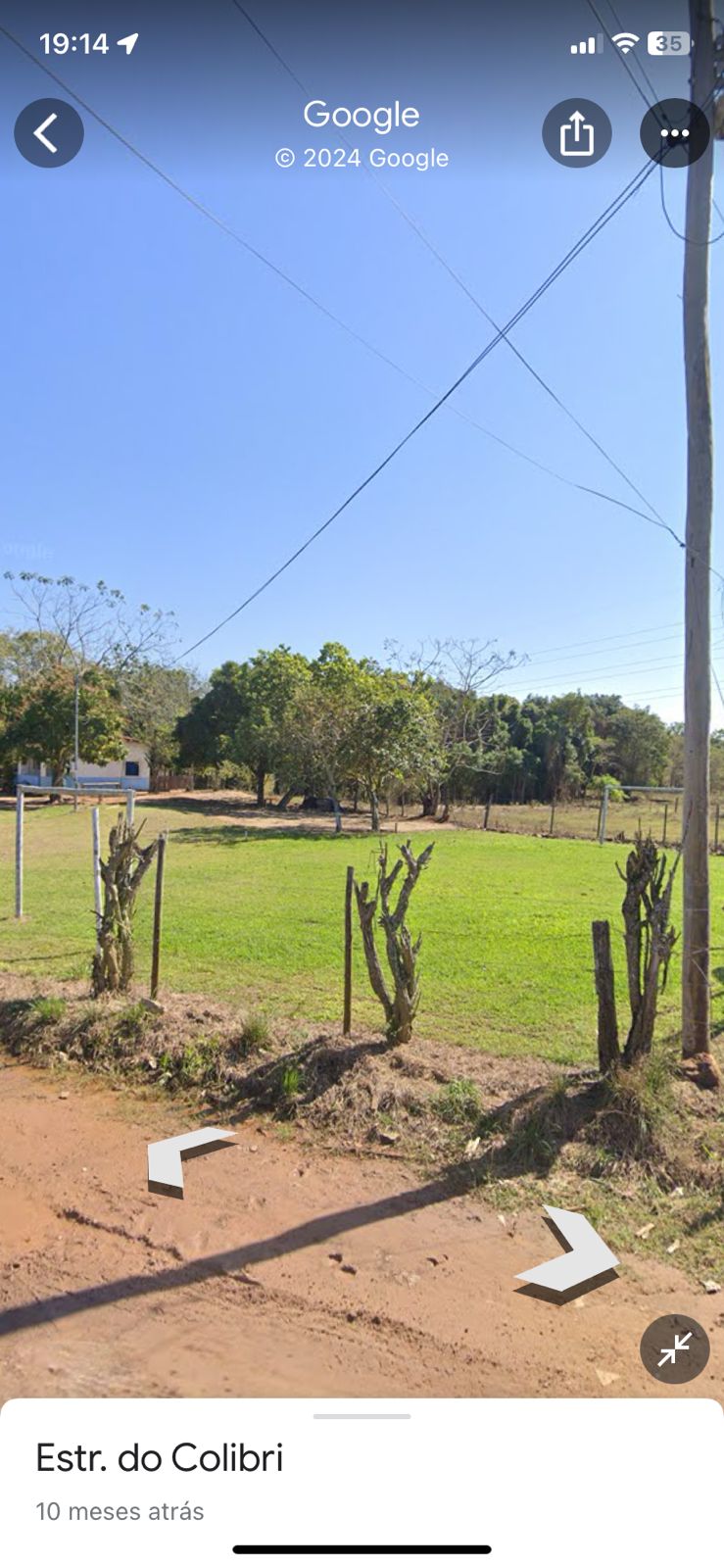 A clear view of an open landscape is presented, featuring grassy areas and a few scattered trees. Fencing lines the perimeter, with several cacti visible in the foreground. Power lines stretch across the sky, adding to the rural setting.
