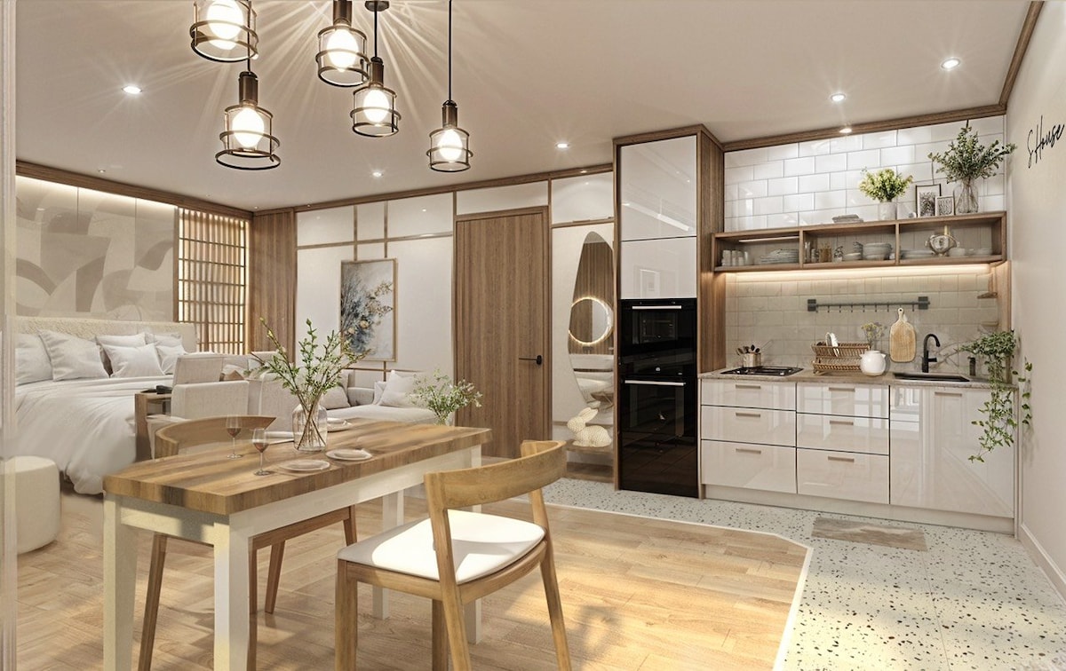 An open-concept living space features a stylish dining area with wooden furniture, a modern kitchen with sleek cabinetry, and soft lighting from pendant fixtures. The ambiance is complemented by light wood floors and artistic decor, enhancing the overall comfort and functionality of the area.