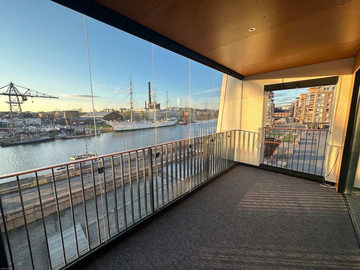 An expansive balcony offers unobstructed views of the river and surrounding area, with glass railings allowing for an open feel. Natural light floods the space, enhancing the smooth flooring and clean lines of the modern design.