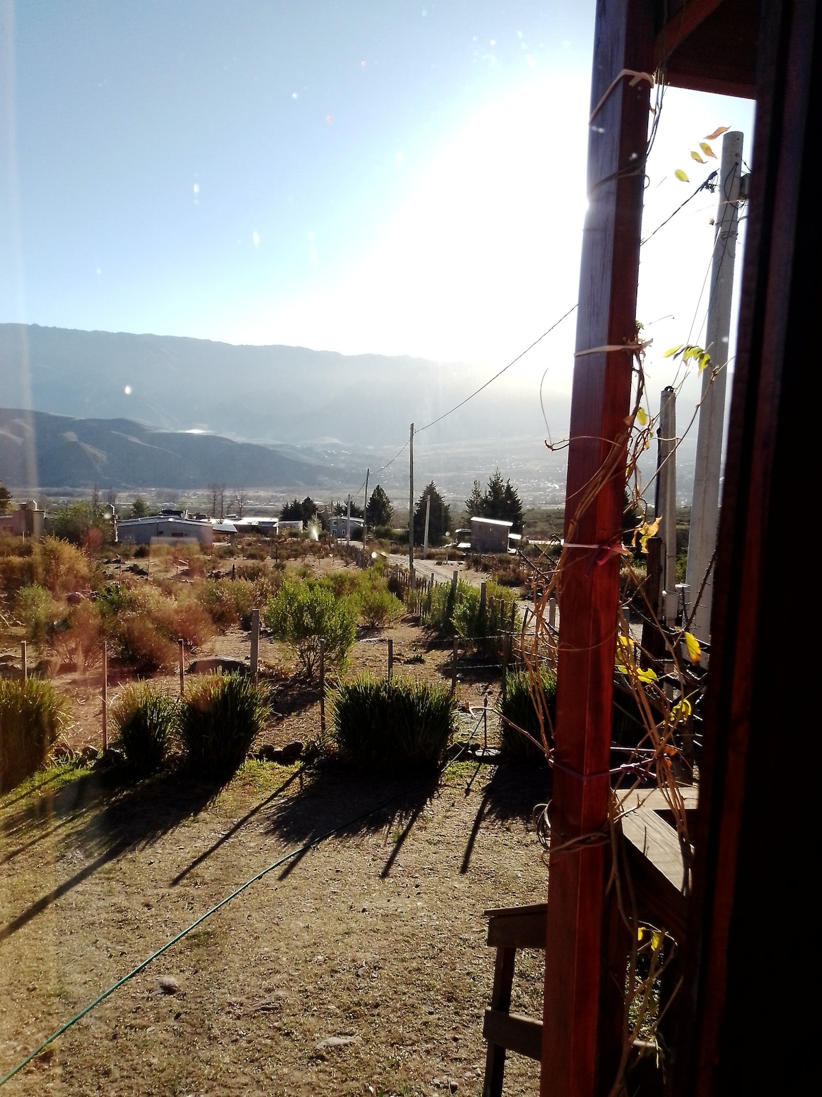 A serene outdoor view is presented from the cabin, showcasing rolling hills and a valley. Sunlight gently illuminates the landscape, highlighting greenery and natural features. Fences and utility poles are visible, contributing to the rustic setting.