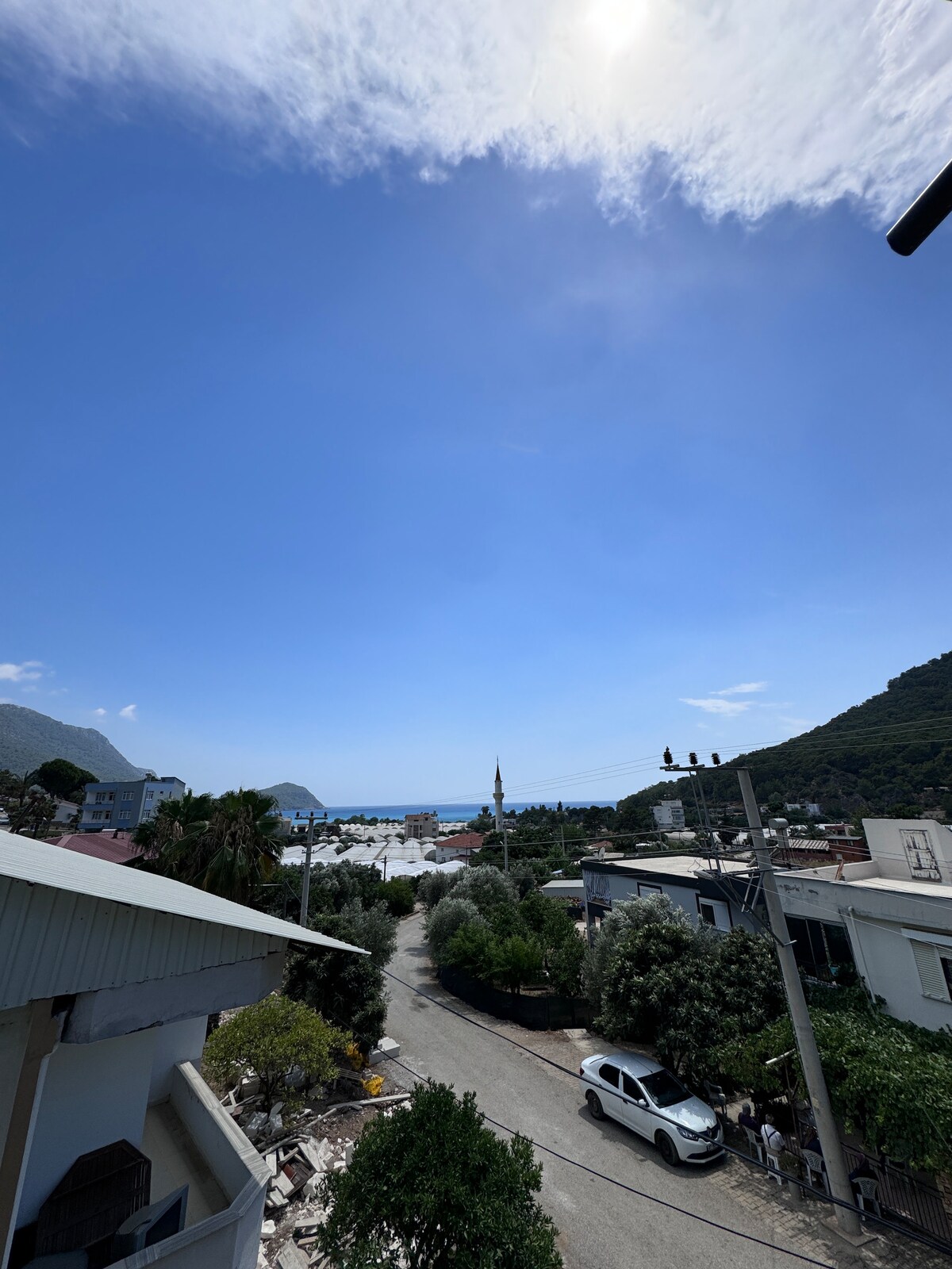 A scenic view from the second floor captures a clear blue sky and distant mountains. The coastline is visible, framed by a peaceful neighborhood with trees and houses. A quiet street leads toward the ocean, enhancing the serene atmosphere of the location.