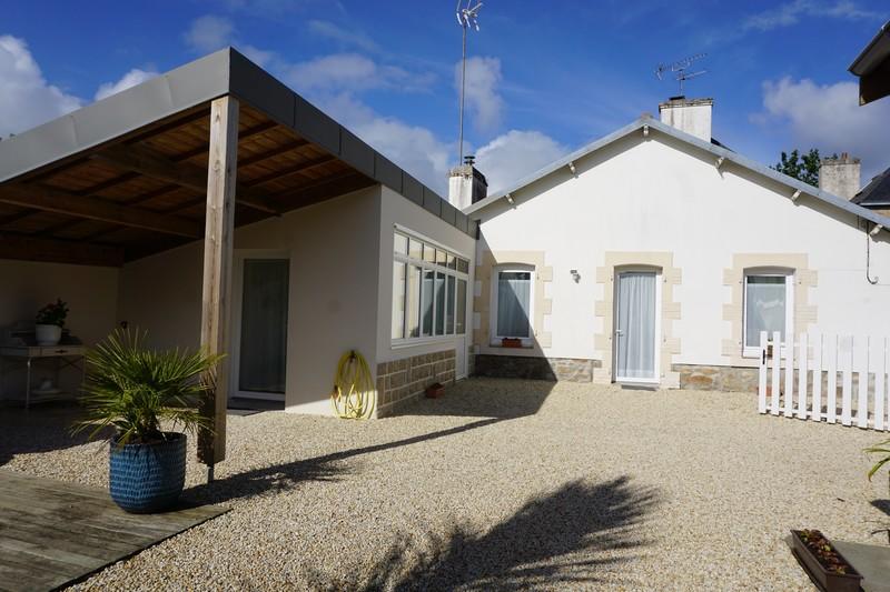 A renovated single-story house is presented with a welcoming facade. The exterior features a gravel courtyard, surrounded by greenery, a sheltered area, and a bright sunlit space with large windows. The setting promotes a sense of relaxation and connection to the outdoors.