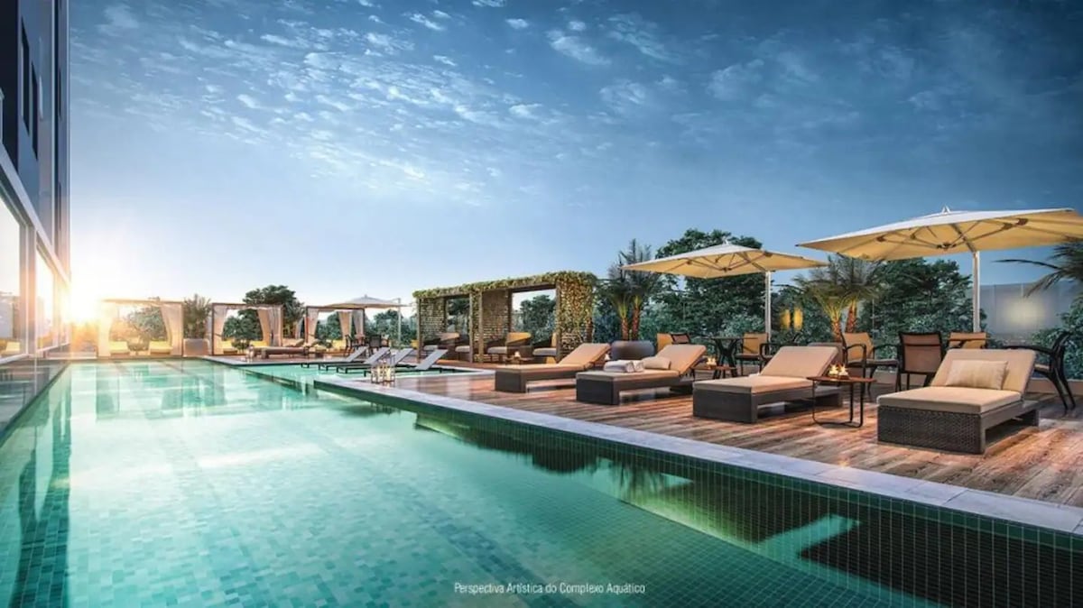 An inviting pool area is observed, featuring a long swimming pool bordered by lounge chairs and umbrellas. Lush greenery surrounds the space, complemented by the warm glow of the setting sun, creating a serene atmosphere for relaxation.