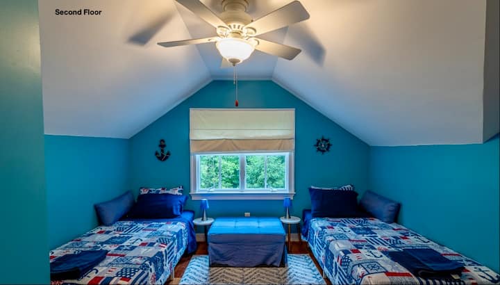 غرفة أطفال بسريرين متماثلين وفراش أرضي واحد قابل للطي مخفي في المقعد العثماني الأزرق