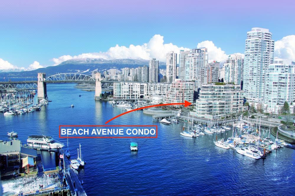An aerial view captures the Beach Avenue Condo positioned along the waterfront, with sailboats nestled in the marina. The backdrop features the city skyline, including high-rise buildings, and the nearby Granville Bridge. The overall scene underscores a serene urban setting near water.