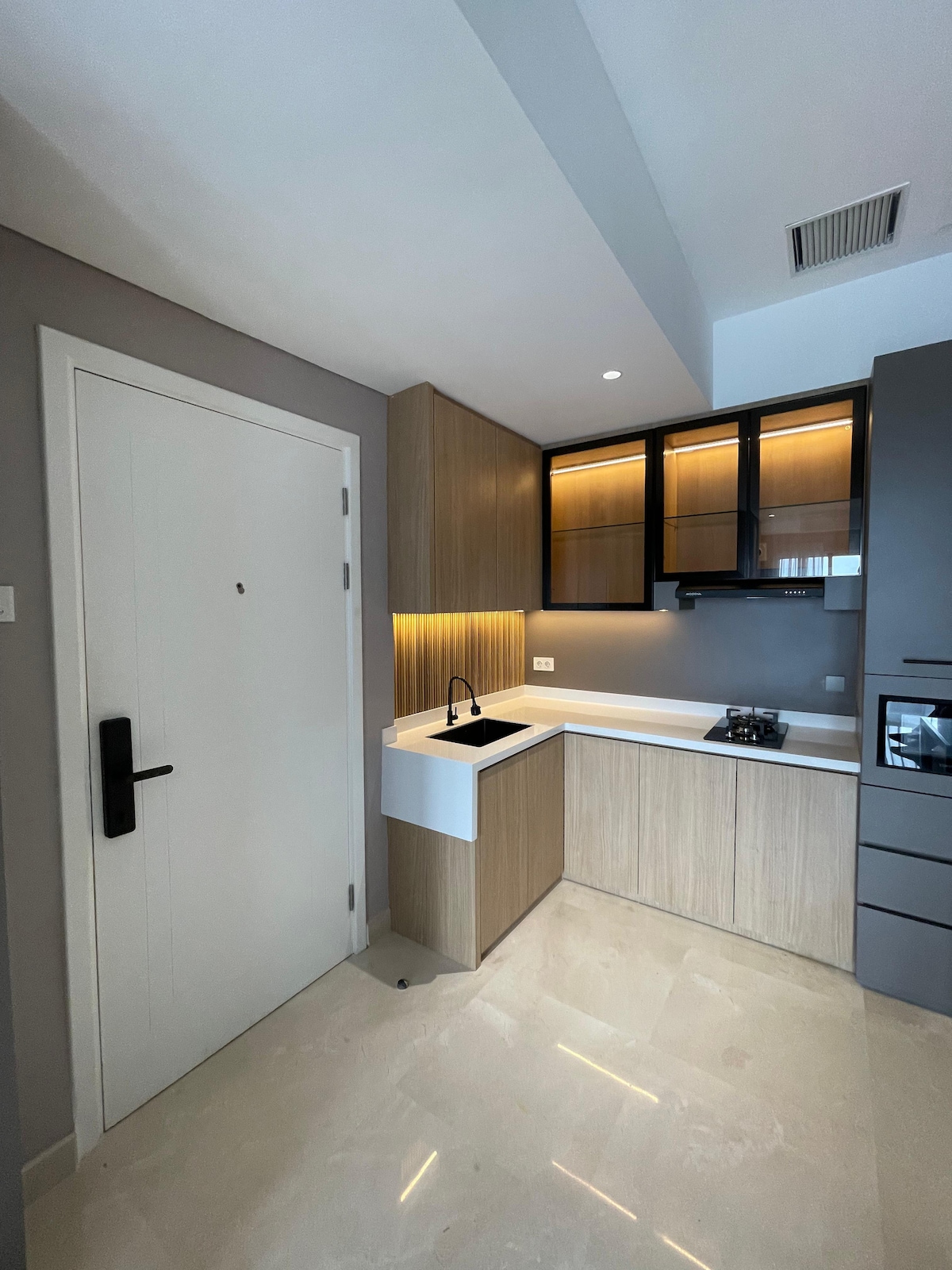 A modern kitchen space is highlighted by a smooth, minimalist design featuring wood cabinetry and sleek countertops. A black sink is positioned beside a gas stove. Subtle lighting enhances the space, creating a functional area for meal preparation. The floor has a glossy, light-colored finish.