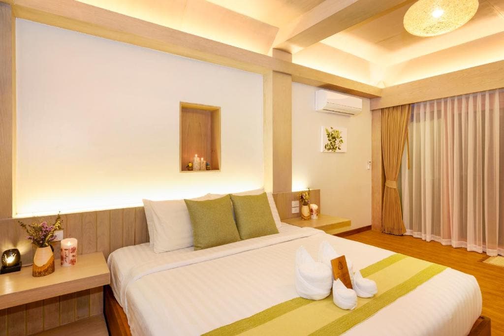 A spacious bedroom is present, featuring a large bed with neutral bedding and accent pillows. Soft lighting highlights the room's features, including a small shelf with decorative items. Floor-to-ceiling curtains frame a large window that allows ample natural light.