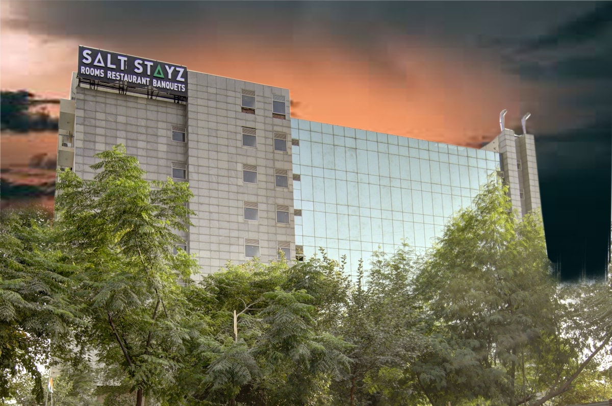 The exterior of the building features a modern façade with large glass windows reflecting the sky. Surrounding trees provide a green contrast to the structure, enhancing the overall appearance. The establishment's name is displayed prominently at the top, indicating the available services.