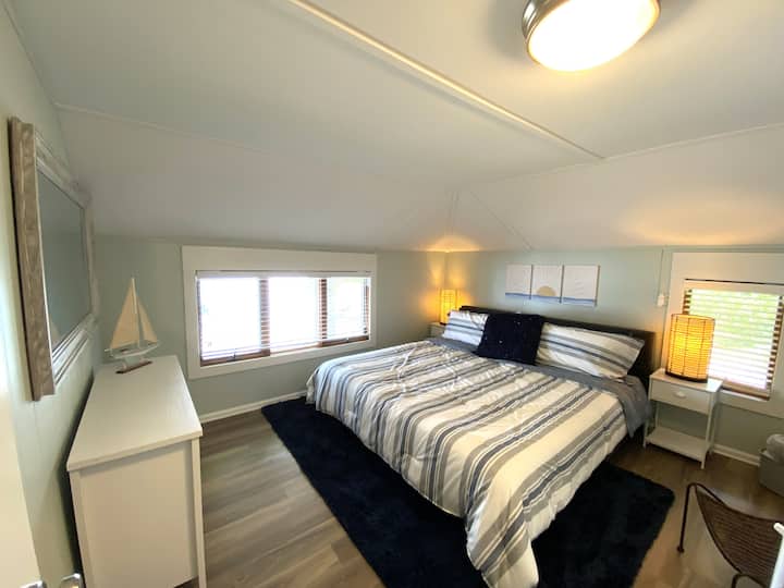 Suite principale accueillante avec literie confortable et vue sereine sur le lac. Cette chambre dispose d'un lit king size, d'une commode, d'une chaise, de tables d'appoint, d'un grand miroir et d'un placard. Il y a des stores sur les fenêtres (pas de rideaux occultants).