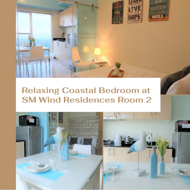 The image displays a coastal-themed room with a calming color palette. It features a spacious bed with fresh linens, a convertible sofa bed, and a kitchen area equipped with modern appliances. A large window offers natural light and a view of the outdoors.