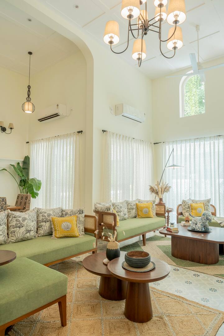 A bright and inviting space with tall windows that bathe the room in natural light. The elegant chandelier, curated décor, and plush seating with cheerful accents create a perfect blend of comfort and charm—ideal for relaxing or entertaining.