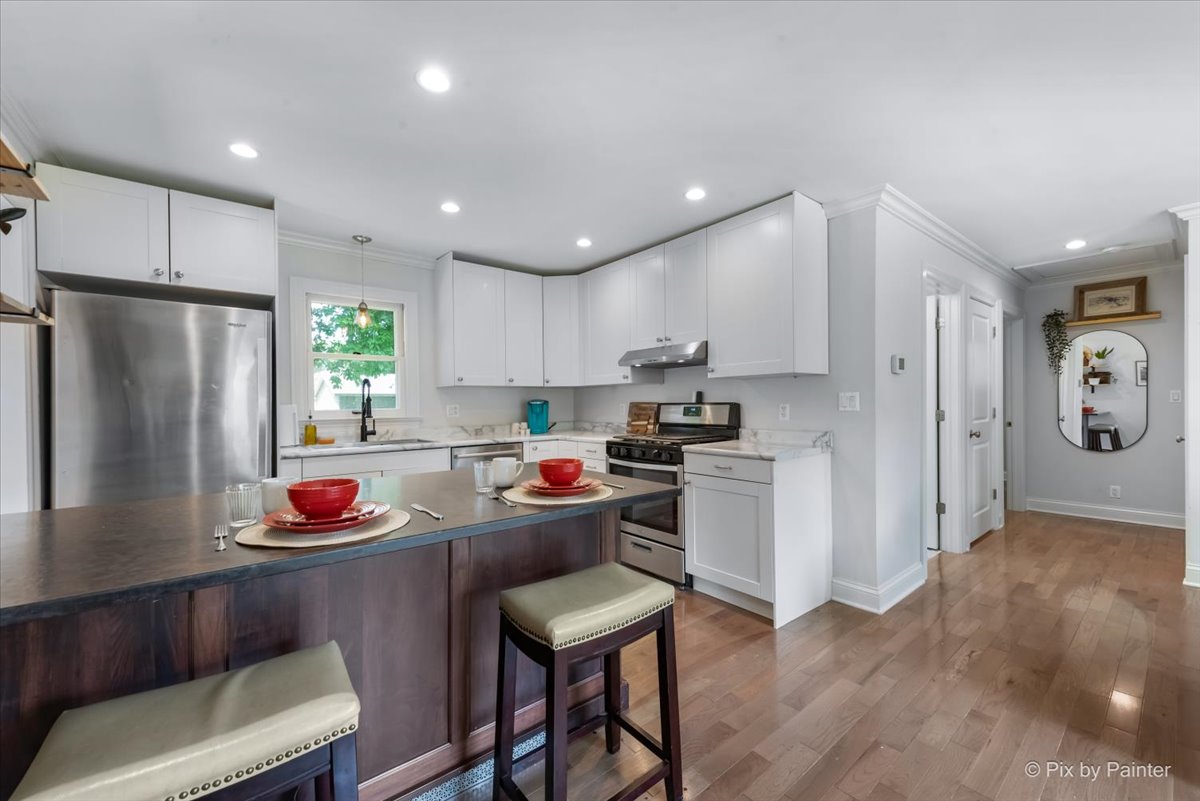 The kitchen features modern cabinetry and stainless steel appliances, including a stove and refrigerator. A spacious island with bar stools provides seating for two. Natural light streams through the window, illuminating the clean, open layout that invites cooking and gathering.