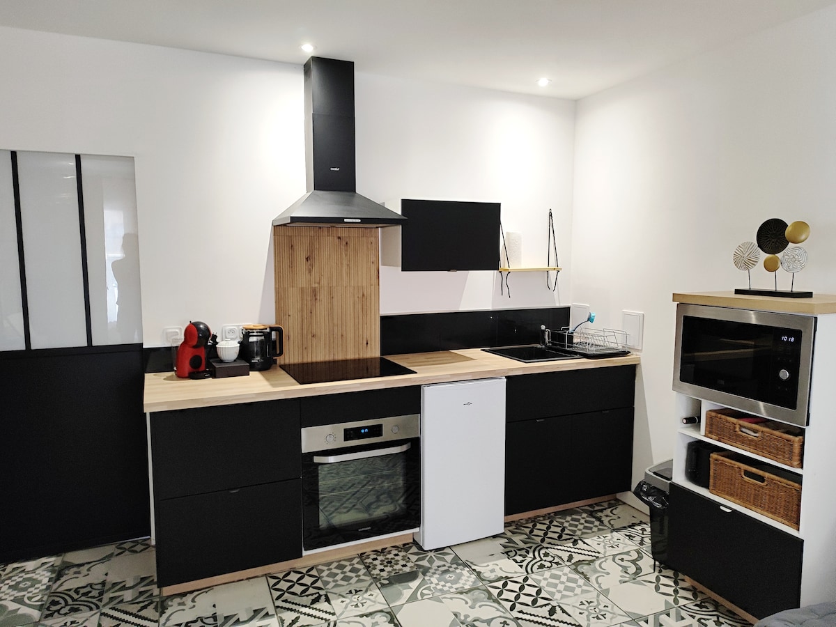 A modern kitchen is presented with sleek black cabinetry and a wood-accented countertop. Essential appliances, including a stove, oven, refrigerator, and microwave, are visible. Decorative details, like a small arrangement on the shelf and patterned flooring, enhance the functional space.