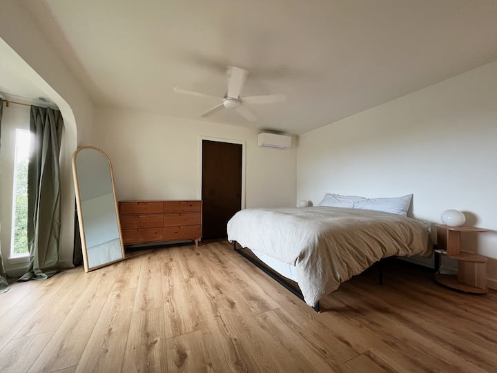 Dormitorio principal grande con ropa de cama tamaño king, ventilador de techo y aire acondicionado.