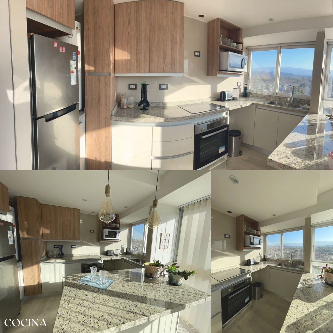 The modern kitchen features contemporary wood cabinetry and a spacious granite countertop. Large windows provide views of the surrounding landscape, while ample natural light highlights the appliances, including a refrigerator, stove, and microwave. Decorative elements, such as small plants, enhance the overall design.