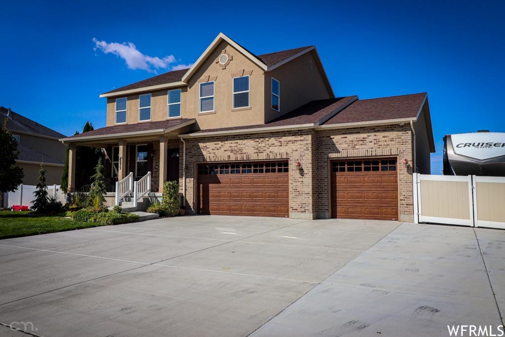 A two-story home features a combination of brick and stucco exterior, complemented by a symmetrical facade. The property includes a spacious driveway leading to a three-car garage with wooden doors. Lush landscaping frames the entrance, enhancing the welcoming appearance.