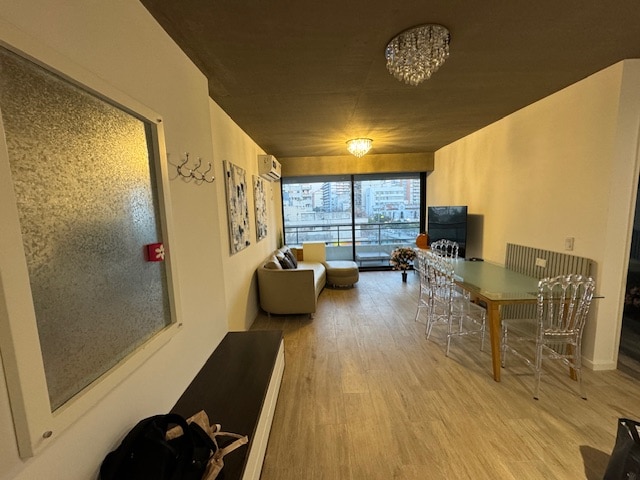 A modern living area is presented with a large window allowing ample natural light. A comfortable sofa is positioned nearby, complemented by a glass dining table with multiple transparent chairs. A flat-screen TV is mounted on the wall, enhancing the space's functionality.