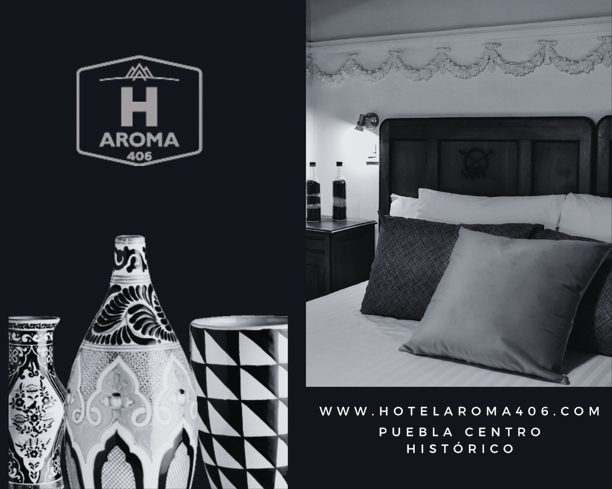 A collection of intricately designed ceramic vases is showcased beside a comfortable bed adorned with pillows in varying shades of gray. The backdrop features a detailed headboard, indicating a blend of traditional and modern decor. A logo and website information are displayed prominently.