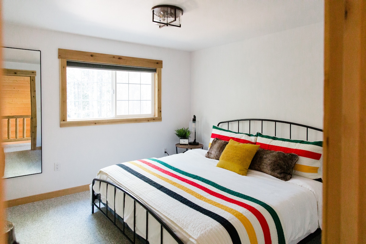 ตู้ลิ้นชักไม้ที่มีเส้นสะอาดวางถาดไม้พร้อมกระถางต้นไม้ หัวกวางตกแต่งสีดำติดตั้งอยู่บนผนังด้านบน หน้าต่างบานใหญ่ที่ล้อมรอบด้วยไม้ช่วยให้แสงธรรมชาติเข้ามาได้ ห้องพักมีเพดานไม้