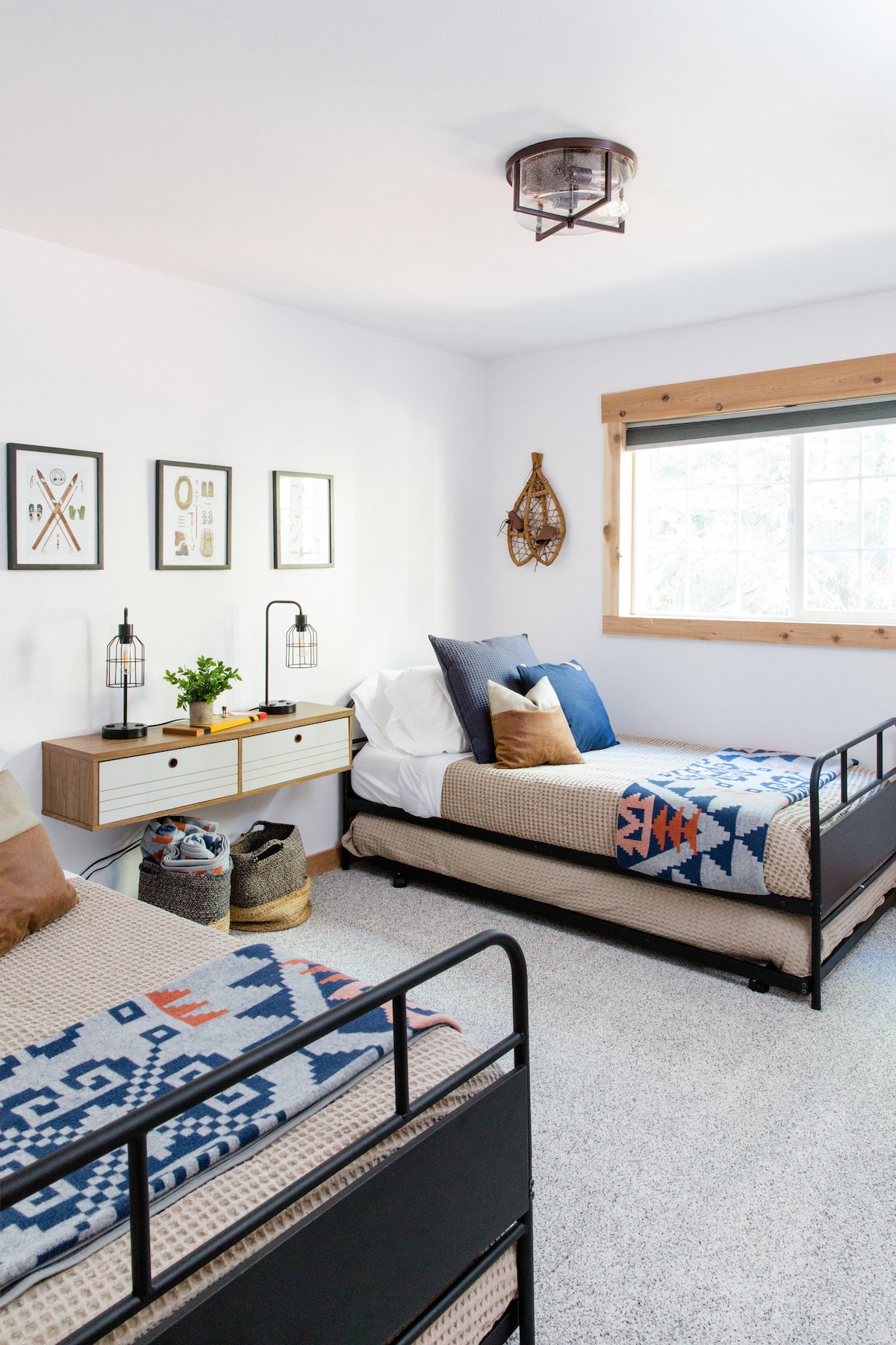 ห้องนอนที่อบอุ่นพร้อมเตียงแฝดที่มีผ้าห่มอุ่นๆและผ้าห่มสไตล์ชนเผ่า การตกแต่งสไตล์ชนบทสมัยใหม่รวมถึงรองเท้าลุยหิมะและงานศิลปะกรอบรูปช่วยเพิ่มเสน่ห์เหมือนเคบินเหมาะสำหรับการพักผ่อนท่ามกลางธรรมชาติ