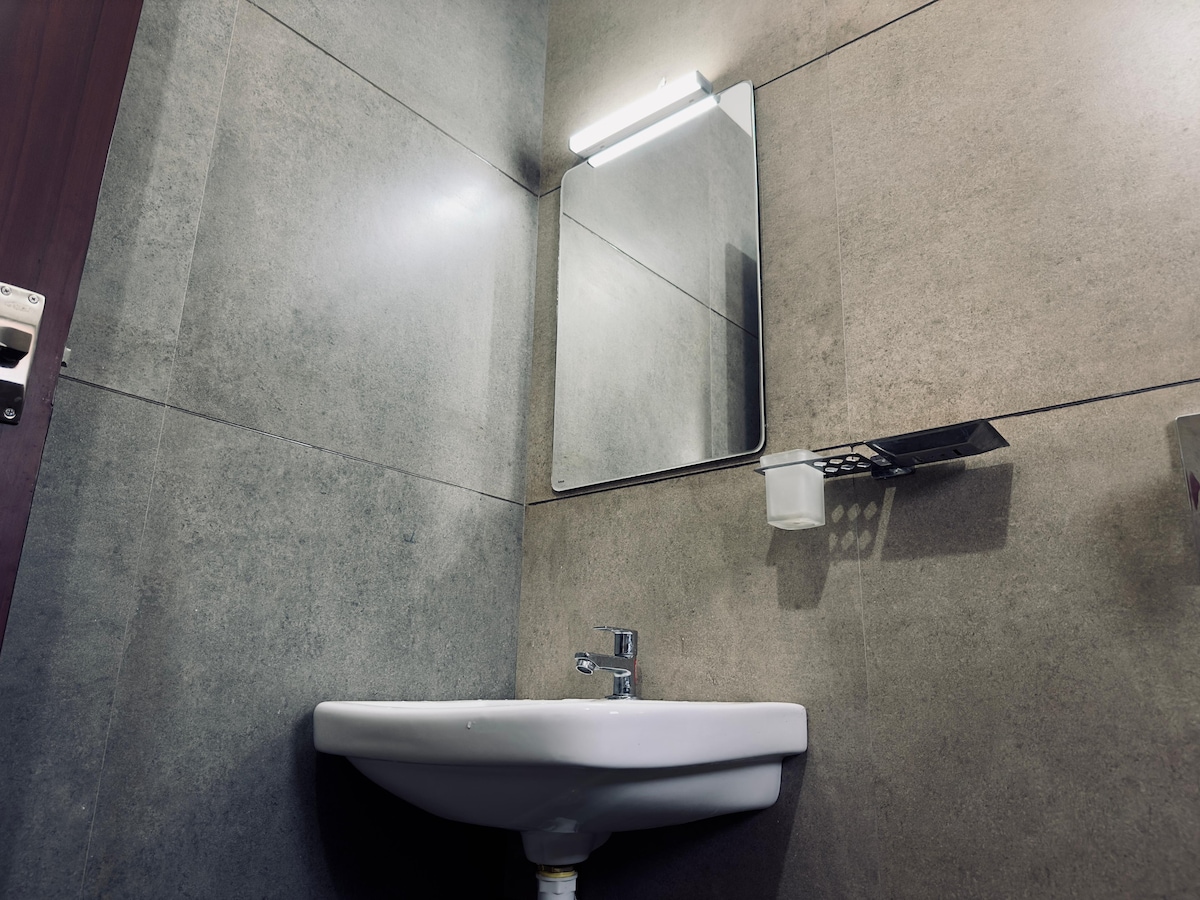 The bathroom features a modern sink with a minimalistic design, accompanied by a mirror mounted above it. Soft lighting enhances the sleek grey wall tiles, creating a clean and inviting atmosphere.