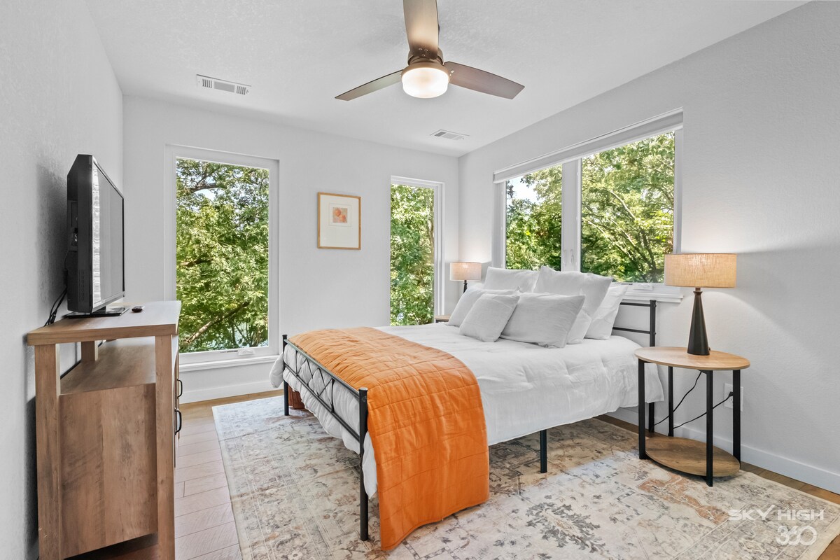 Dormitorio con cama tamaño queen, TV y grandes ventanales con vistas a las copas de los árboles y al lago.  