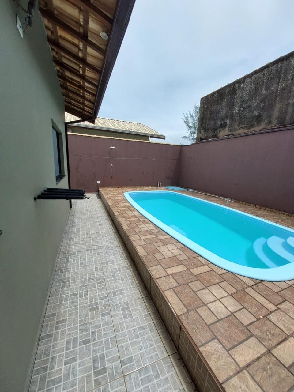 A private swimming pool is situated beside the house, surrounded by a brick patio and enclosed by walls for added privacy. The pool features clear blue water and a gentle curve. Adjacent, a narrow pathway leads to the house's entrance.