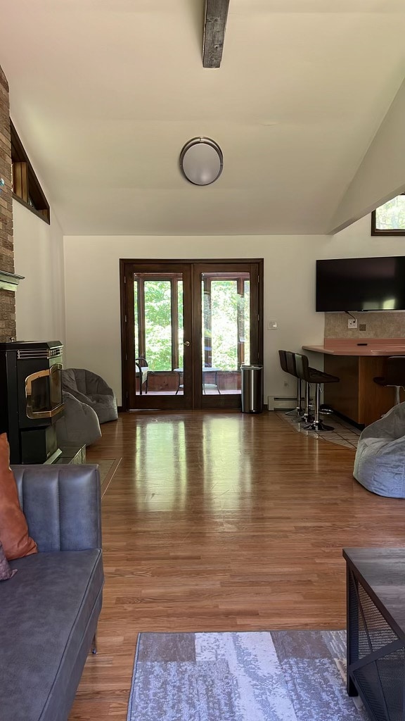 The living area is characterized by warm wooden flooring and an open layout. A cozy seating arrangement with cushioned chairs is complemented by a sleek bar area and a modern TV mounted on the wall. Large glass doors lead to a nature-filled view outside.