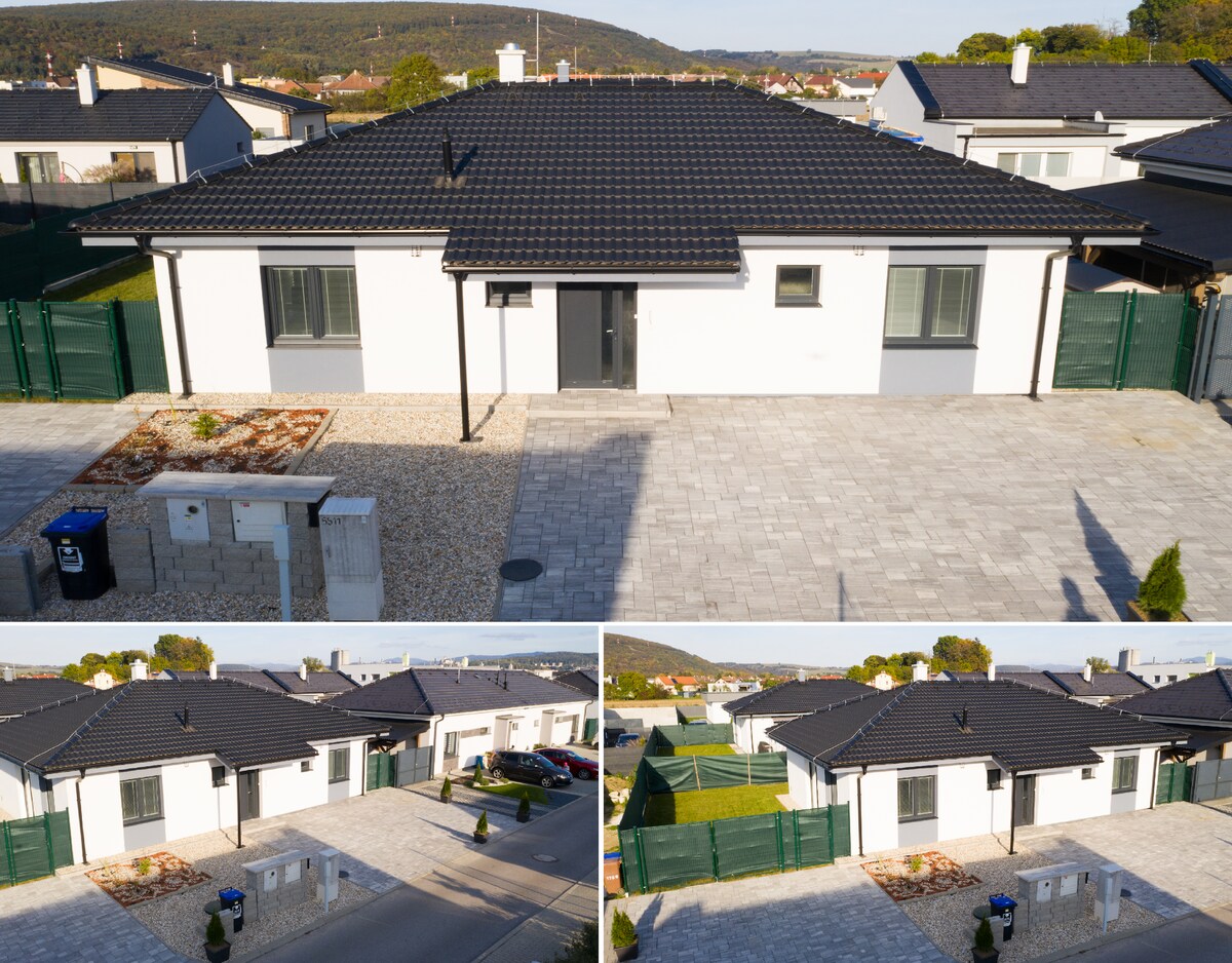 The exterior of the property is showcased with a modern white façade and a dark roof, surrounded by a well-maintained garden. The driveway is paved, with a landscaped area visible in front. A private parking space is also evident.