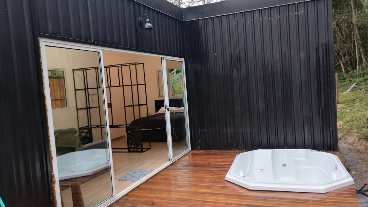 A private outdoor deck features a modern hot tub, surrounded by natural greenery. Large glass doors offer a view into the inviting indoor space, where calming colors create a serene environment.