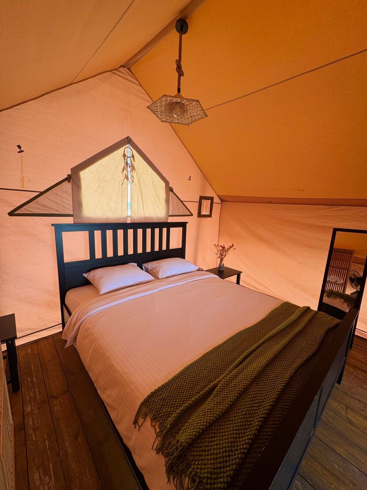 A spacious sleeping area is presented with a wooden bed frame and soft bedding. Natural light filters through a triangular window, casting gentle shadows. A minimalist nightstand stands beside the bed, and a cozy throw blanket is draped across the bed.