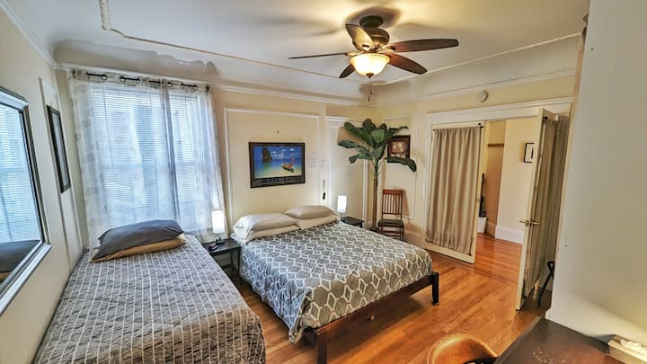 Enorme dormitorio del medio con pisos de madera, una cama tamaño queen y se puede colocar con dos camas individuales adicionales para dormir 4 personas. Tiene un armario, un gran escritorio y una silla para un espacio de trabajo privado y luz natural desde una ventana alta.