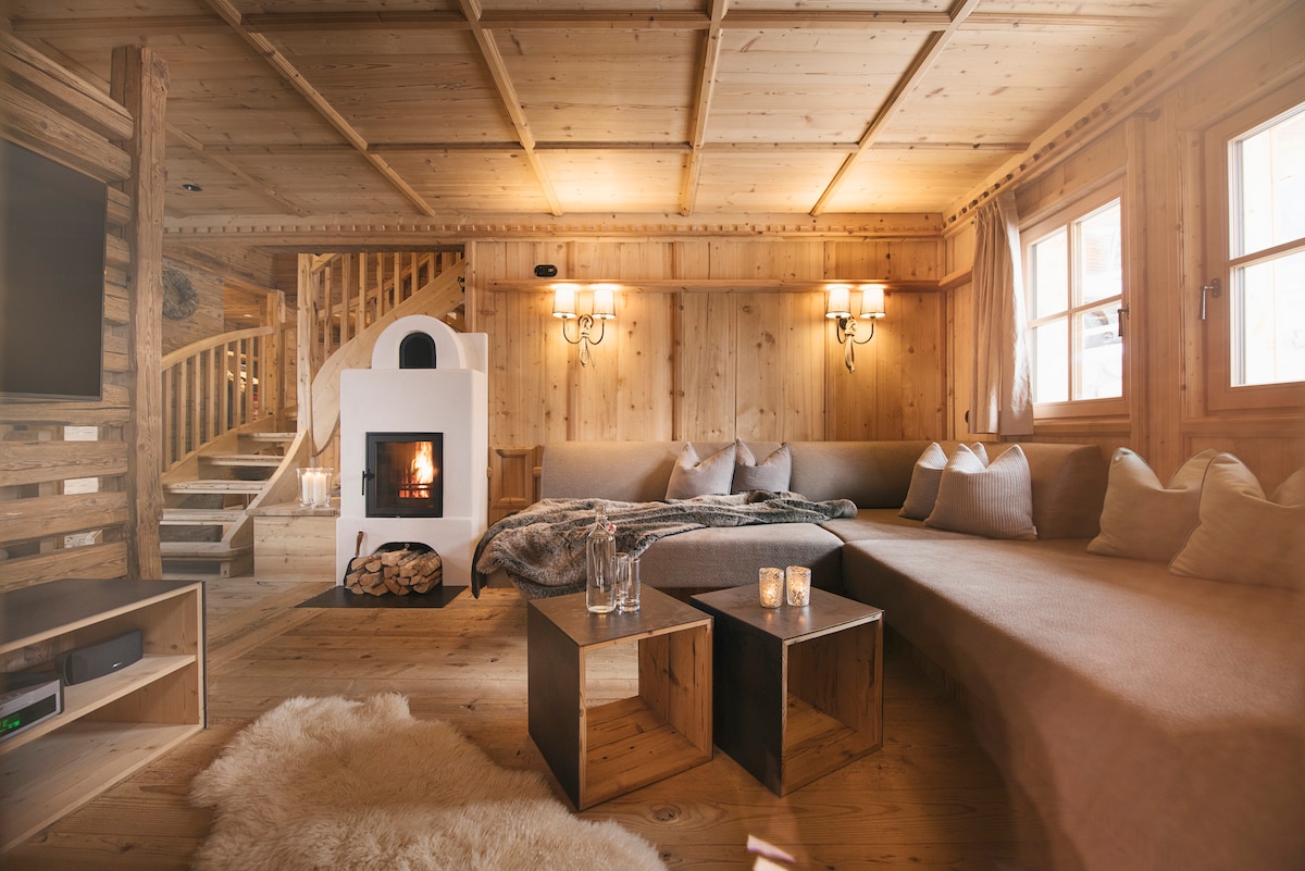 A spacious living area features warm wooden paneling and a cozy fireplace, providing a homey ambiance. Comfortable seating is arranged around modern coffee tables. Soft blankets and cushions enhance comfort, while large windows allow natural light to brighten the space.