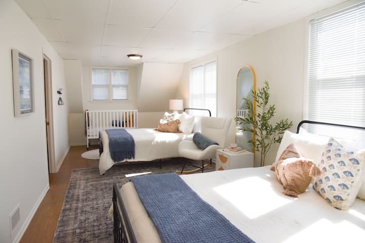 Chambre spacieuse au deuxième niveau avec deux lits queen size, lit pour bébé portable grand format, rocker + tables de chevet avec ports de recharge.